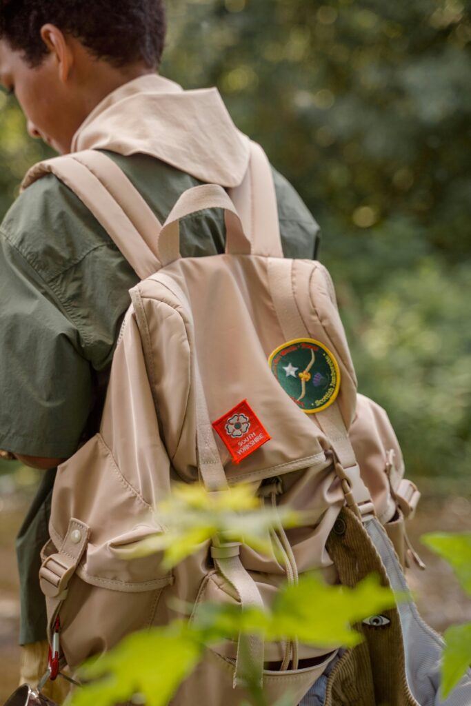 A young scout with a badge-decorated backpack in a forest setting.